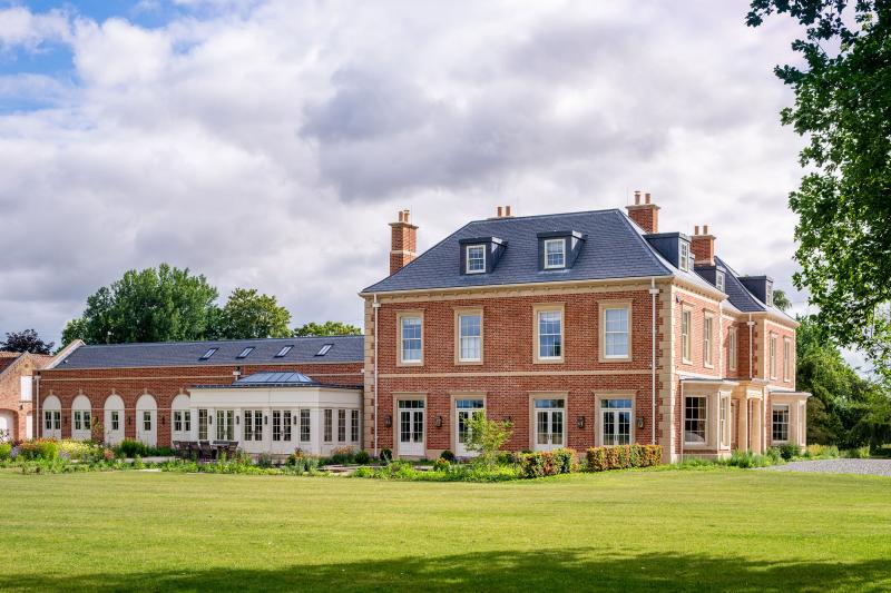 New-build Georgian-style country house featuring red brick, stone quoins and an orangery extension