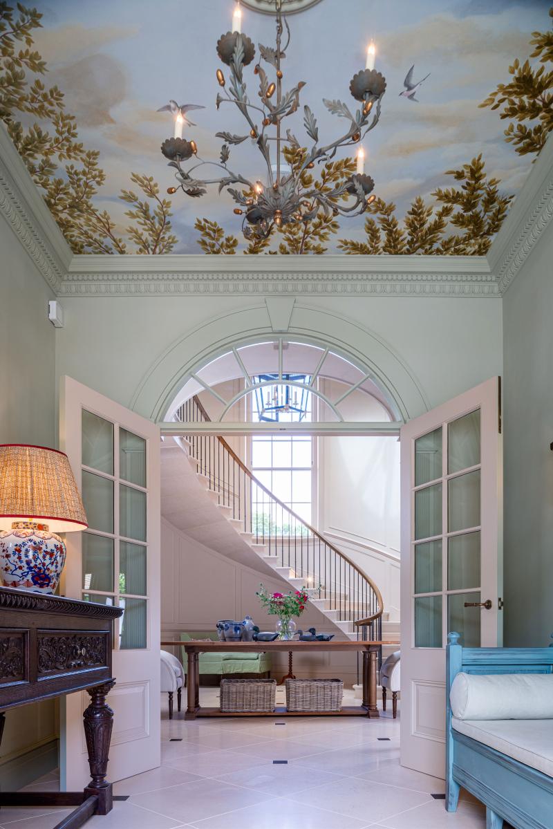 Entrance hall with hand-painted tree and bird ceiling mural, wrought-iron chandelier, and view to a curved staircase