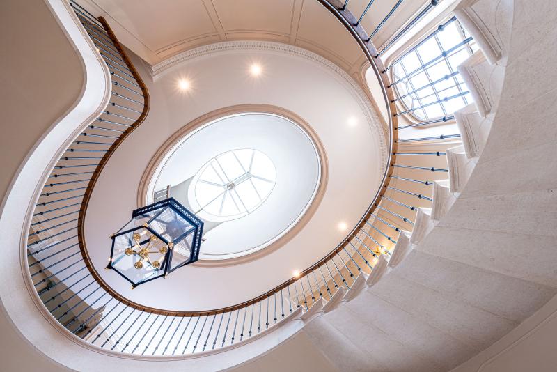 Sweeping curved staircase with wooden handrail and glass lantern light above a panelled entrance hall