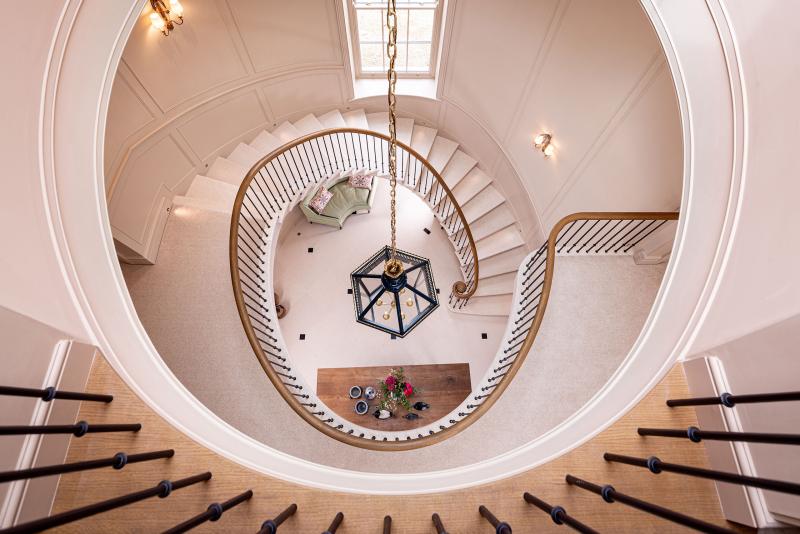 Looking down a curved staircase to a hallway table and green sofa below