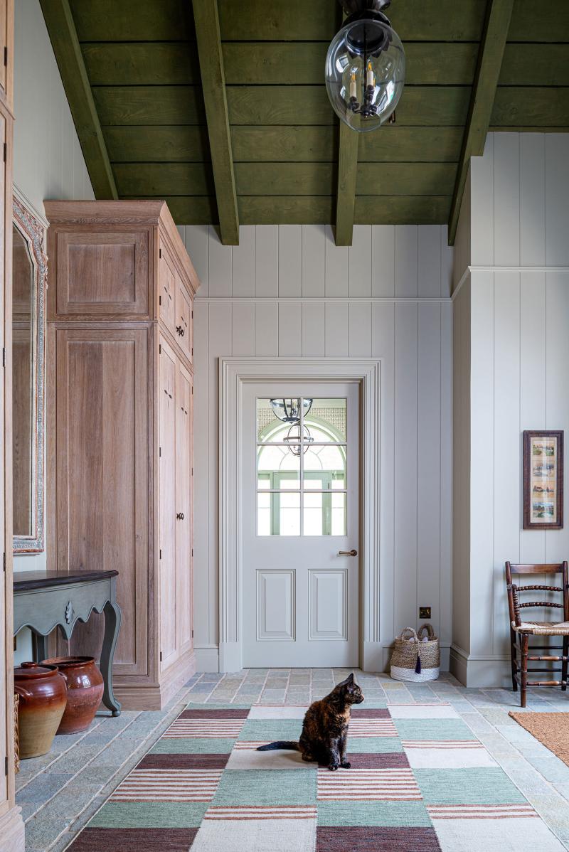 Boot room with green-painted ceiling, oak wardrobe and a cat sitting on a striped rug