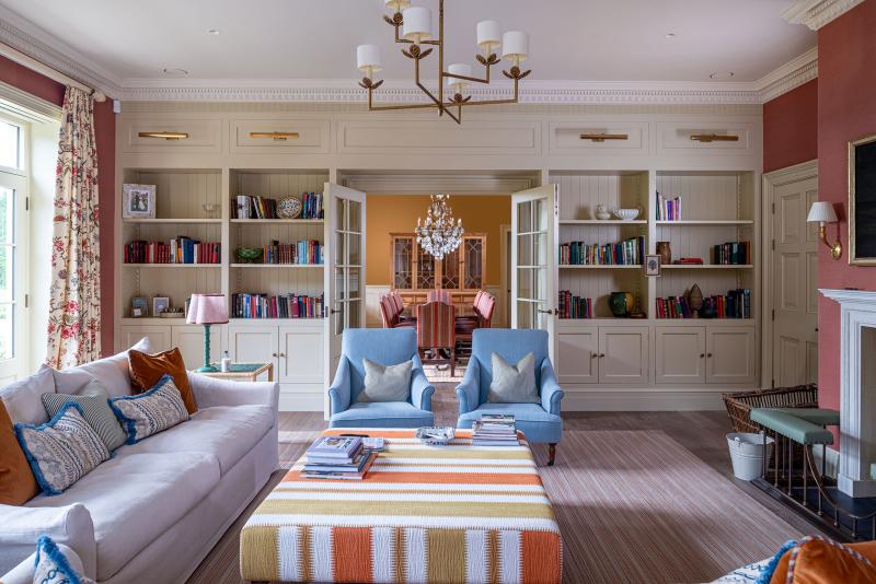 Sitting room with built-in bookshelves and blue armchairs opening onto a dining room beyond